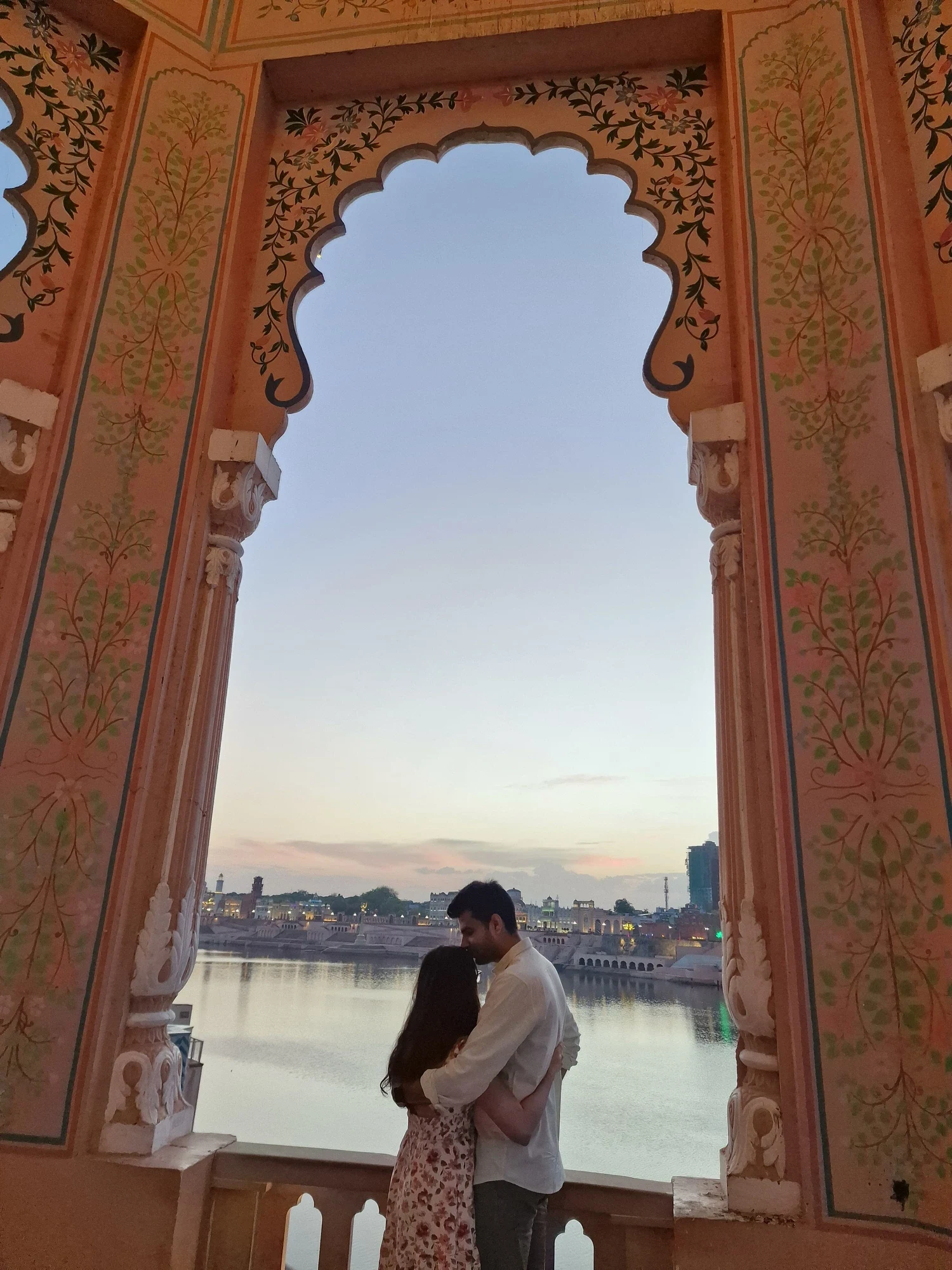 Vijay Laxmi and Dileep framed by a painted haveli arch at dusk